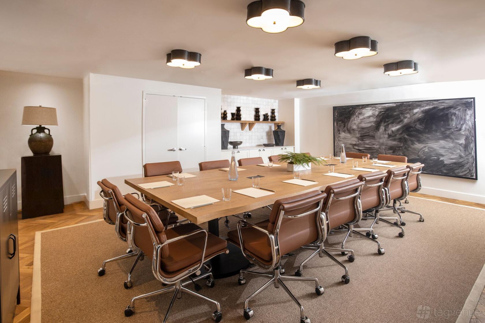 A hotel meeting room with a long wooden table, leather chairs, overhead lights, and abstract wall art at Lyle Washington DC - Lower level.
