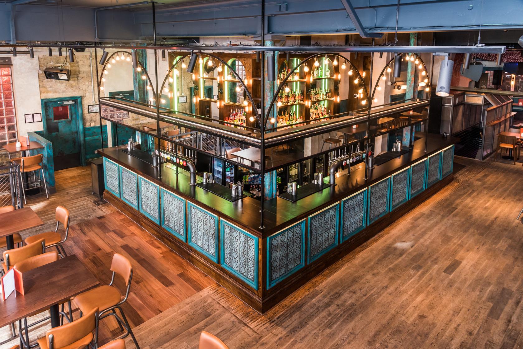 A bar with turquoise paneled counters, exposed bulb lighting, and wooden floors at Big Chill Kings Cross.