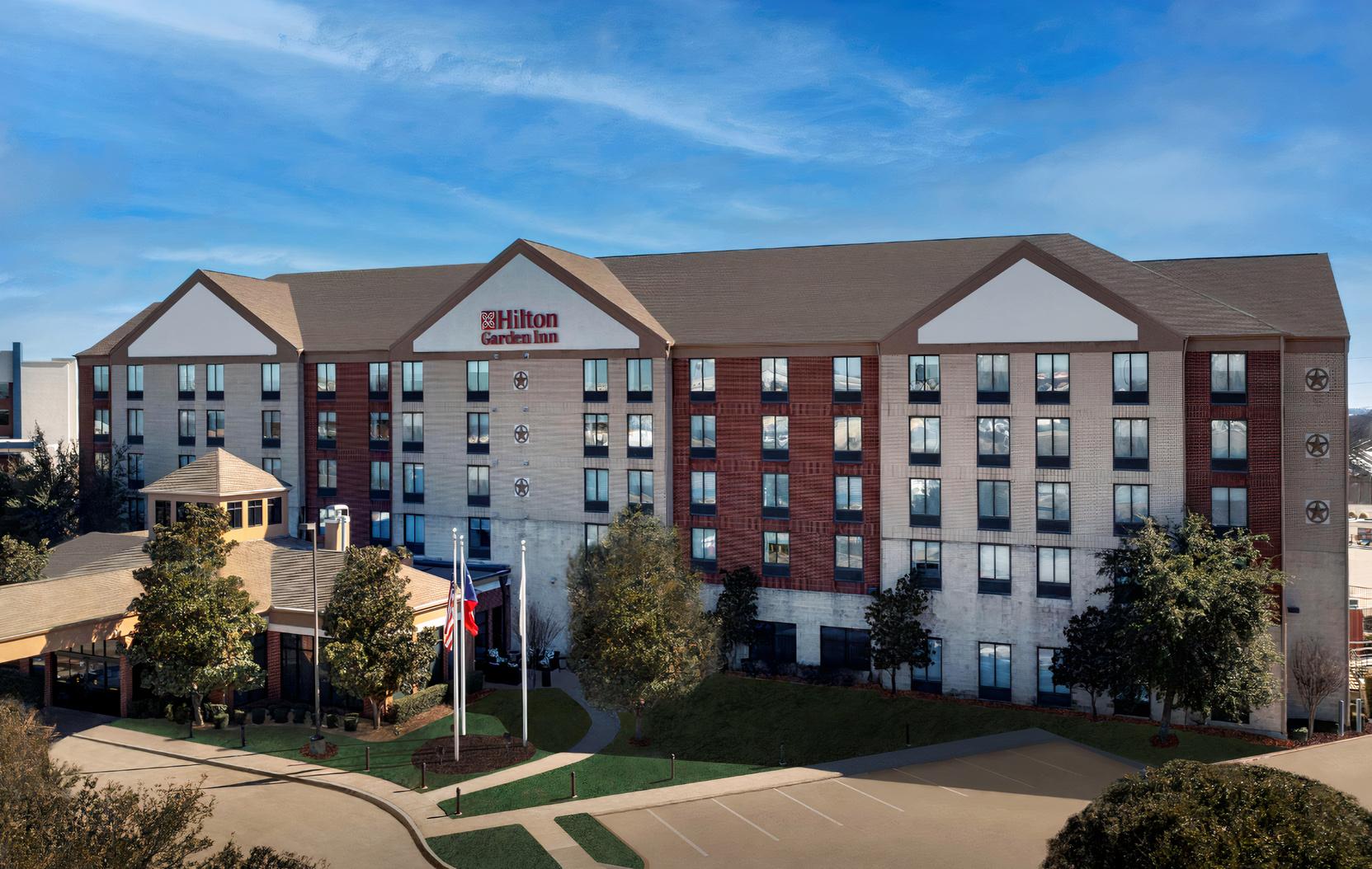A multi-story hotel with red and white facade, large windows, and entrance driveway at Hilton Garden Inn Dallas/Duncanville.