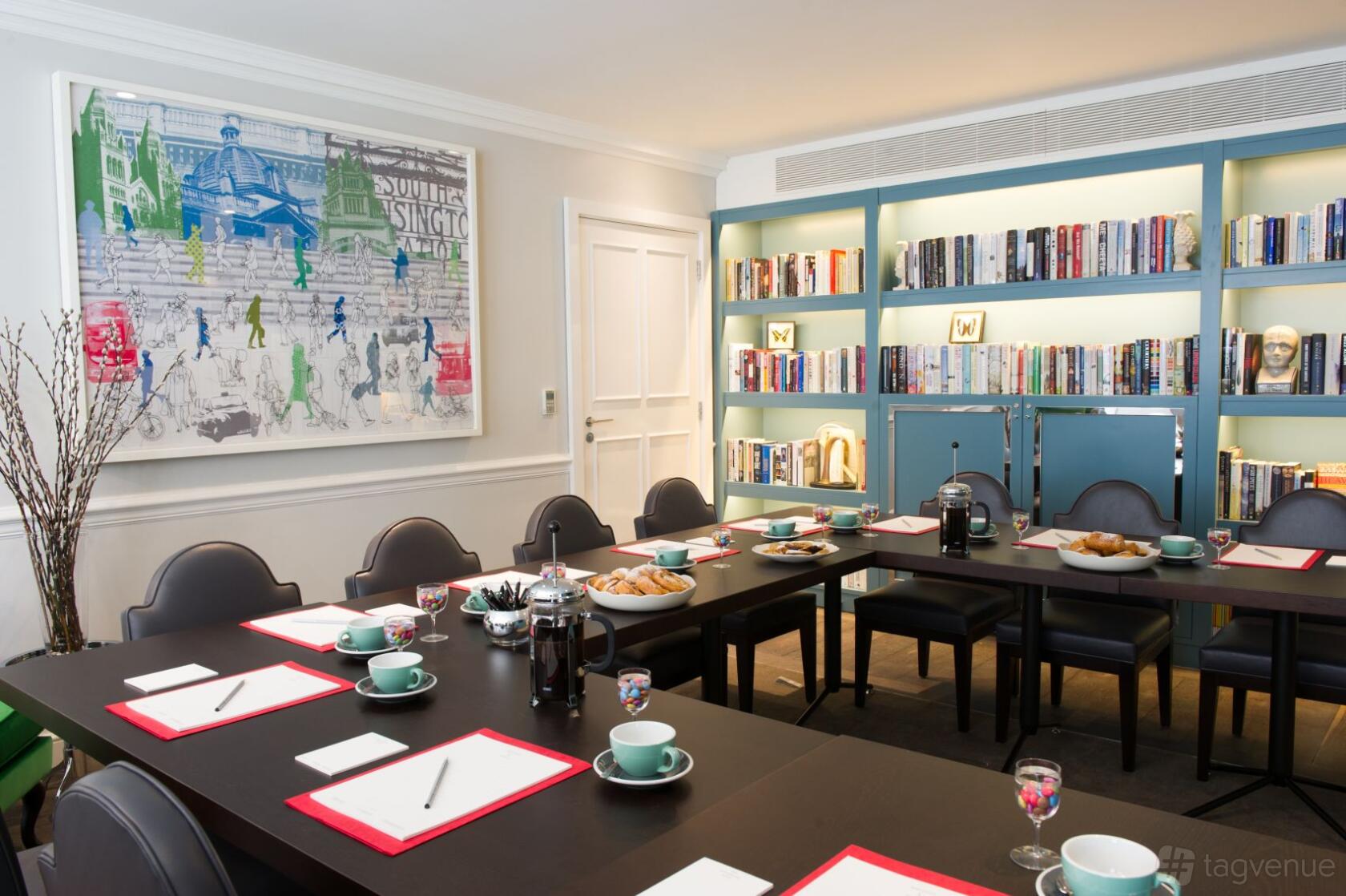 An event space with floor-to-ceiling bookshelves, artwork, and conference tables set for a meeting at The Ampersand Hotel.