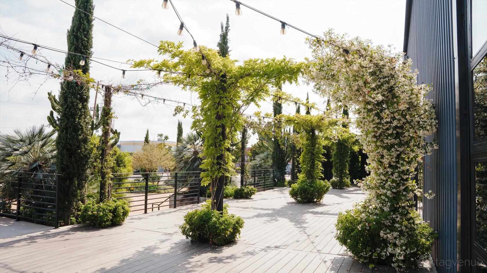 An outdoor event venue with wooden decking, vine-covered pergolas, and string lights at Rolling Greens On Mateo.