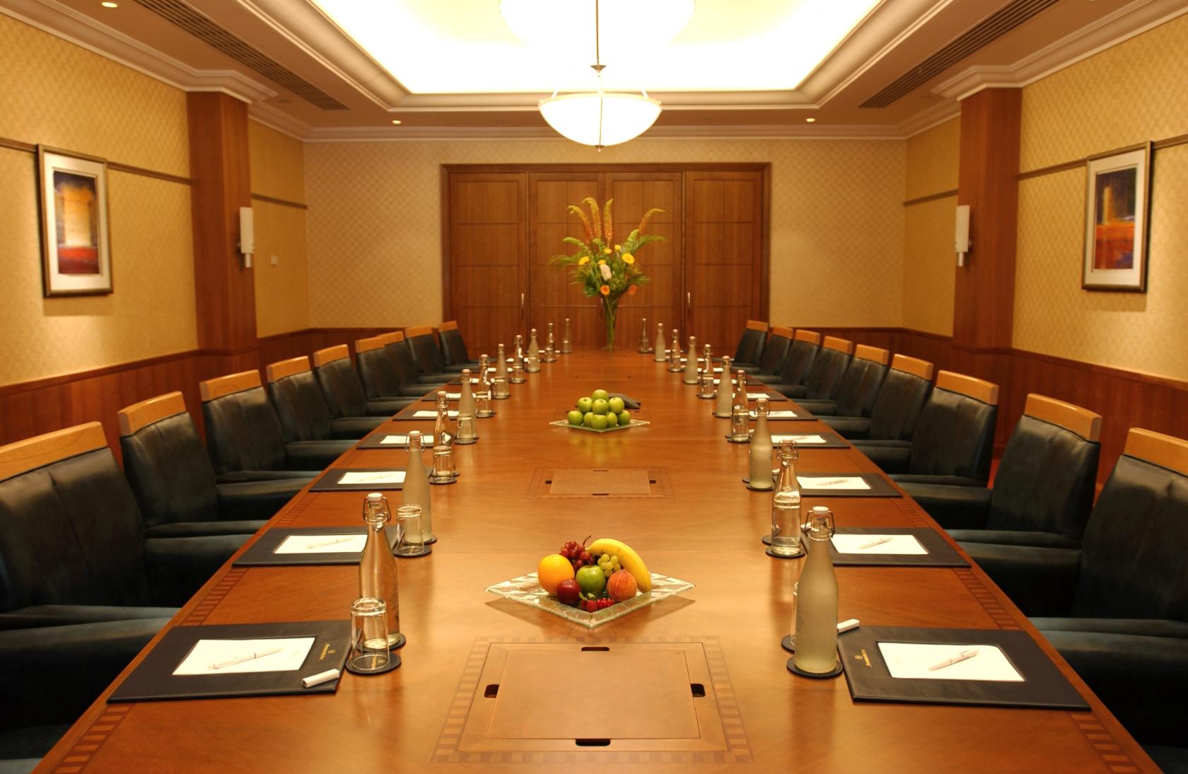 A meeting room with a long wooden conference table, leather chairs, and fruit centerpieces at Sheraton Skyline Hotel London Heathrow.