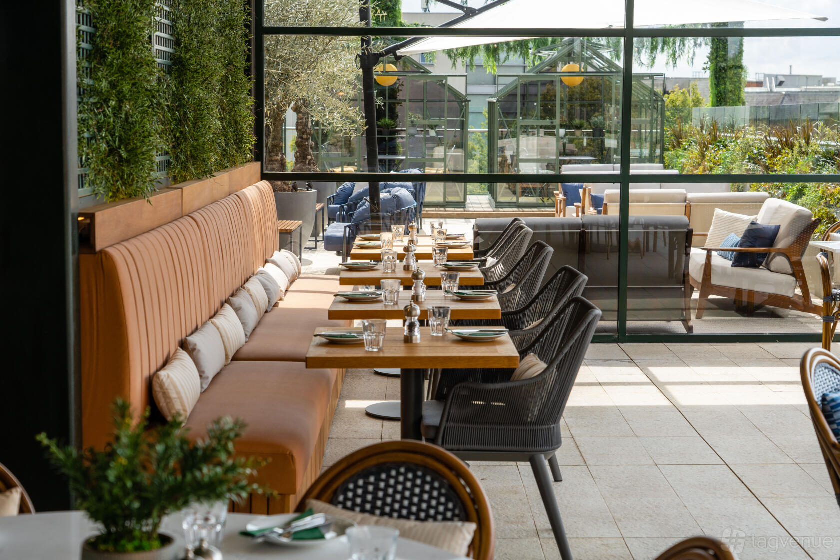 An outdoor cinema space with long cushioned bench seating, wooden tables, and greenery walls at The Light Banbury.