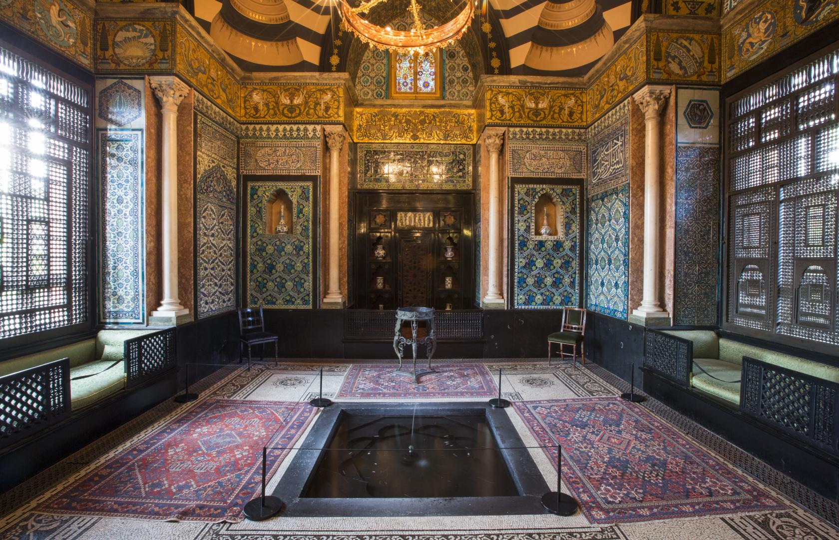 A museum hall with ornate Islamic-style tilework, marble columns, stained glass windows, and mosaic floors at Leighton House.
