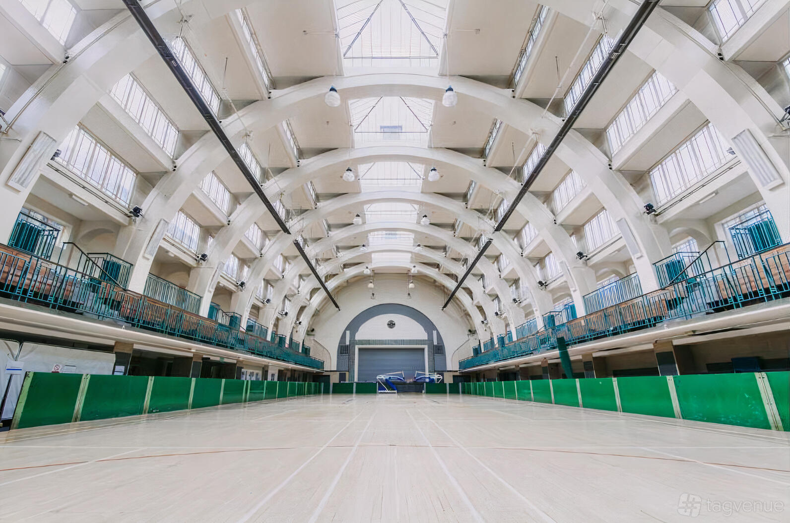A spacious hall with high arched ceilings, skylights, green railings, and a wooden sports floor at Seymour.