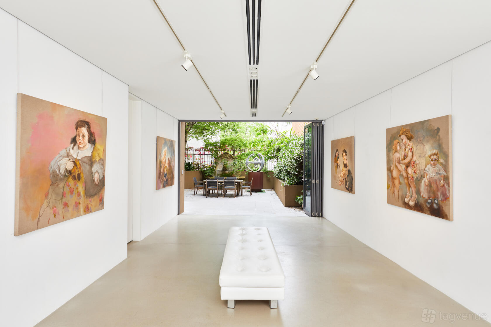 An art gallery event space with white walls, contemporary paintings, and a white bench at Stanley Street Gallery.