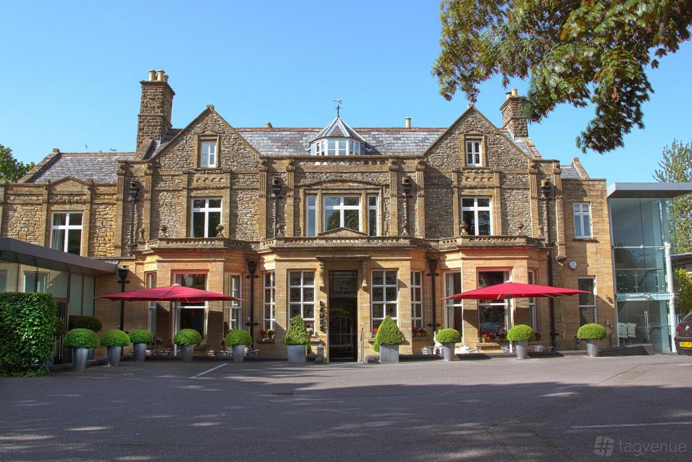 A hotel with a historic stone facade, arched windows, and outdoor seating with red umbrellas at Lanes Hotel.
