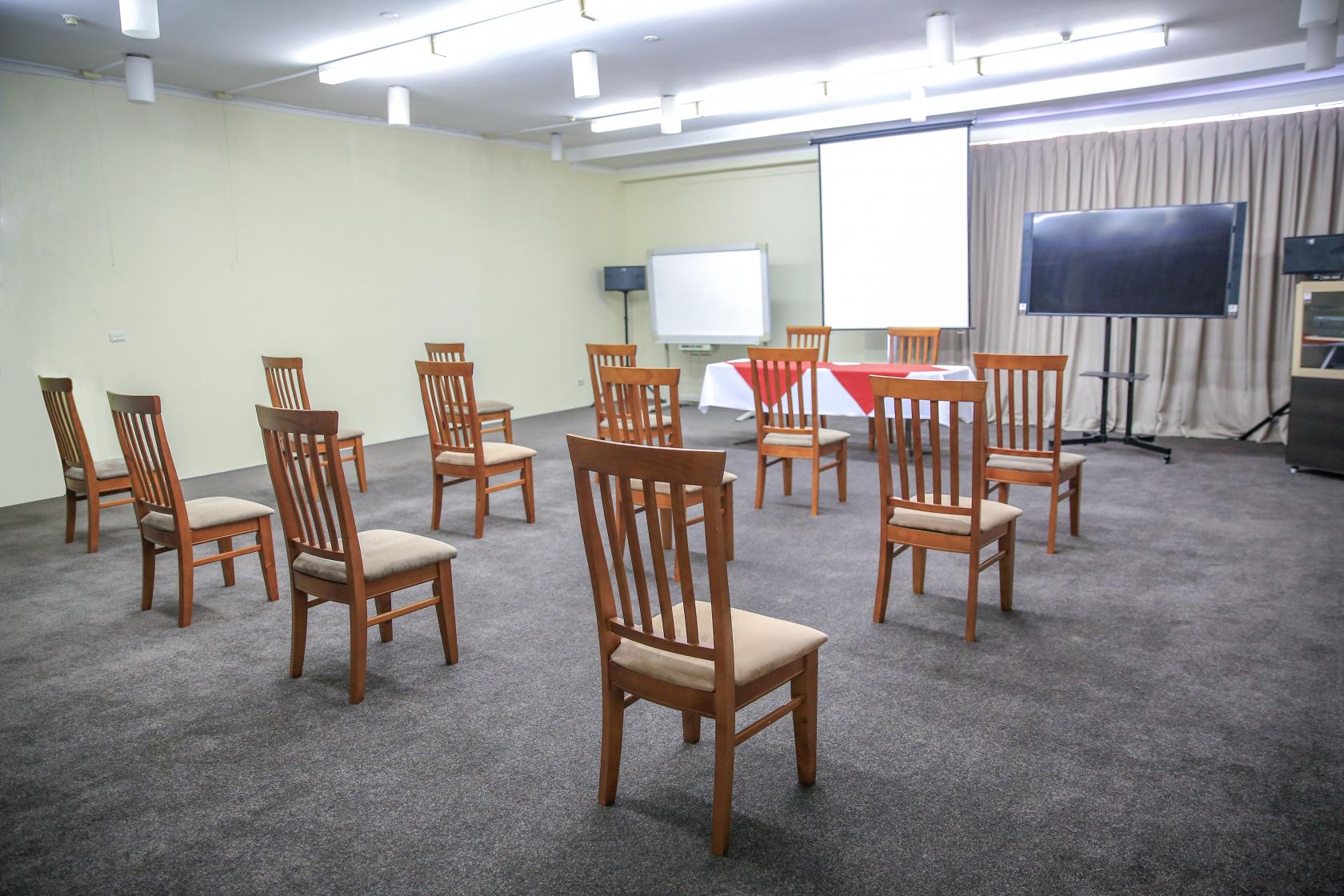 A function room with spaced wooden chairs, a projection screen, whiteboard, and flat-screen monitor at Ryde Inn.