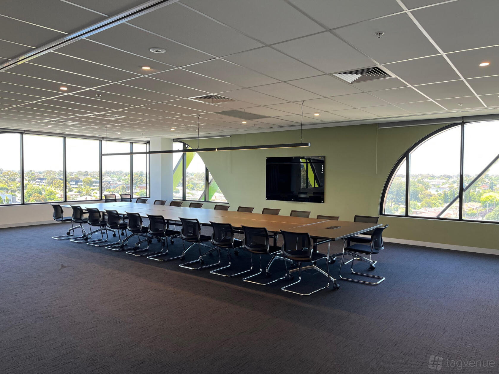 A training room with a long conference table, black chairs, wall-mounted screen, and large windows at The Work Studio.