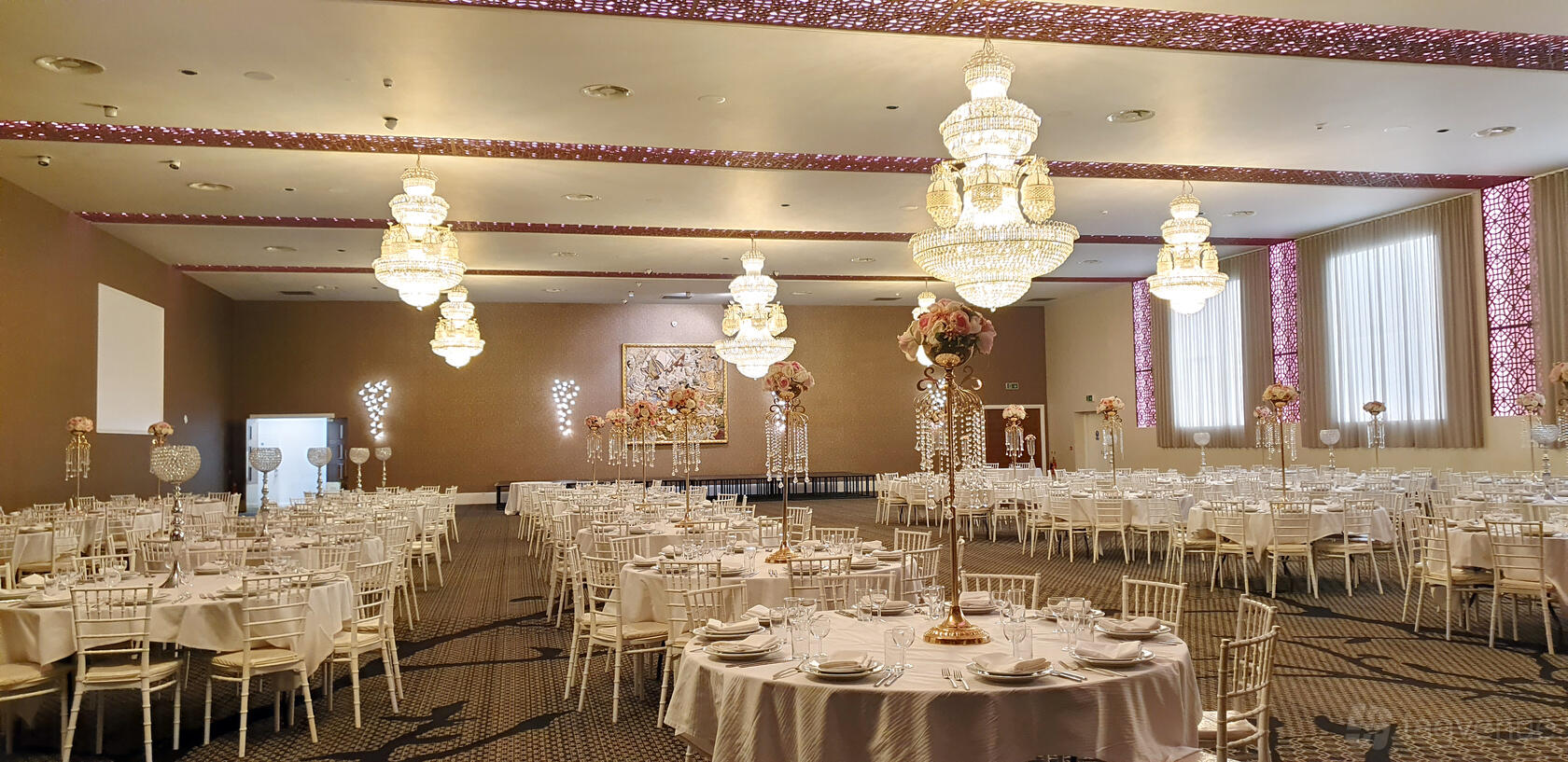 An elegant event space with crystal chandeliers, round tables with white linens, and tall floral centerpieces at Vermilion.