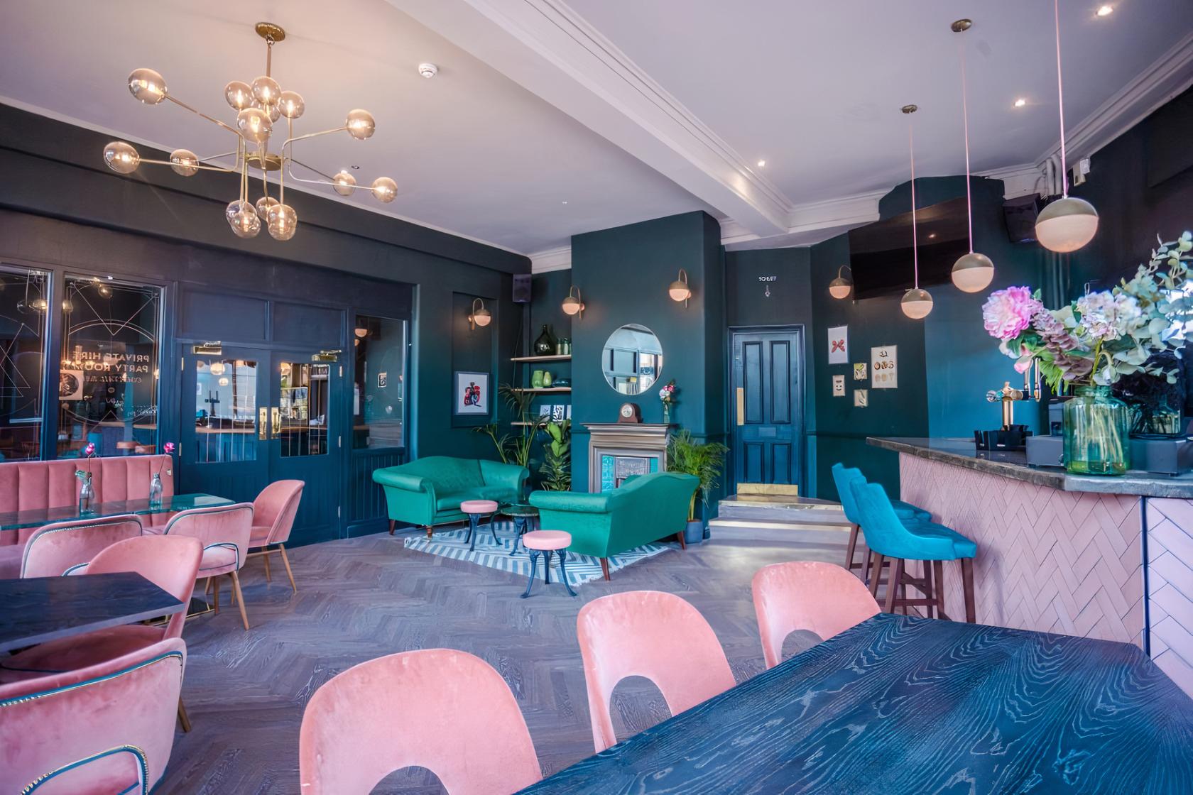 A function room in a pub with pink velvet chairs, round pendant lighting, and green sofas at Heathcote & Star.