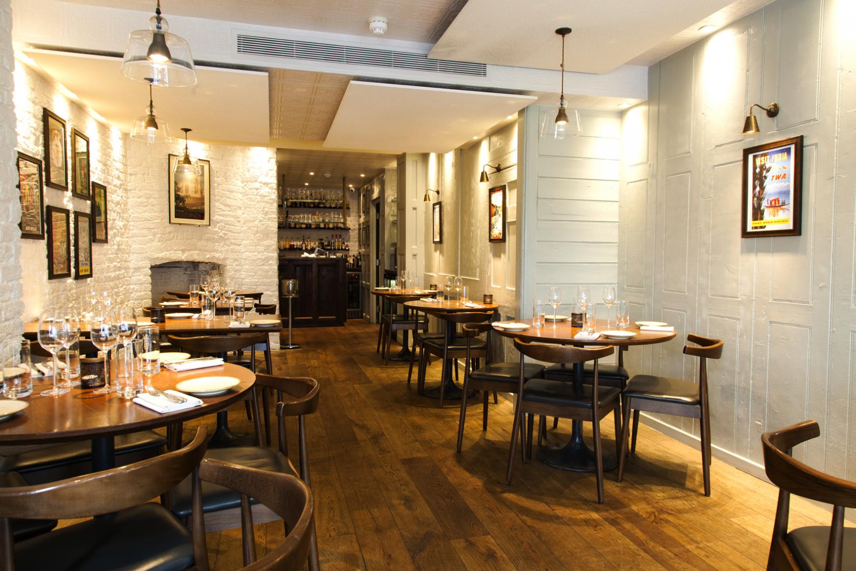 A restaurant with wooden floors, neatly set round tables, and exposed white brick walls at Trishna.