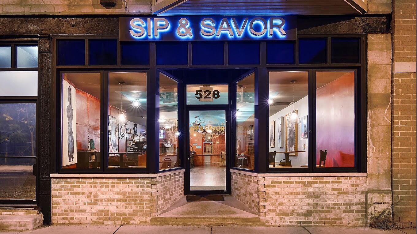 A café with large glass windows, brick exterior, and illuminated sign at Sip & Savor - Bronzeville.