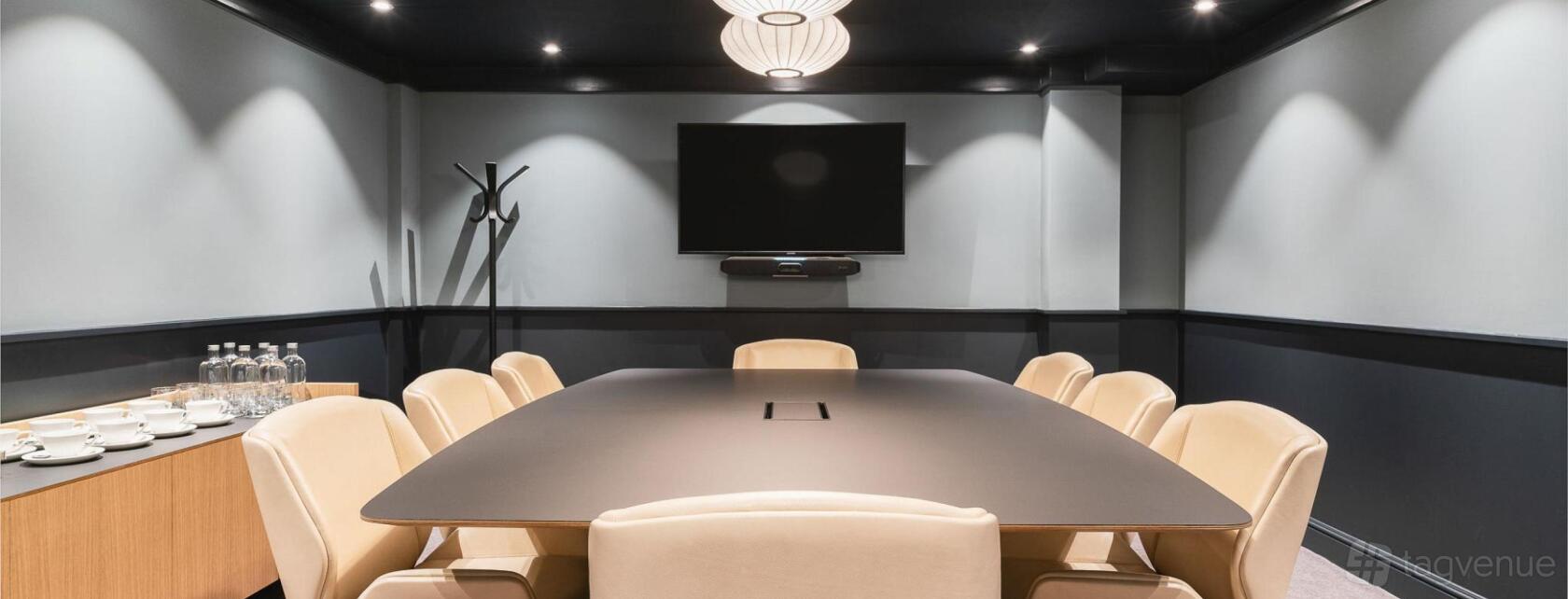 A meeting room with a long conference table, leather chairs, wall-mounted TV, and coat stand at 78-79 Pall Mall.