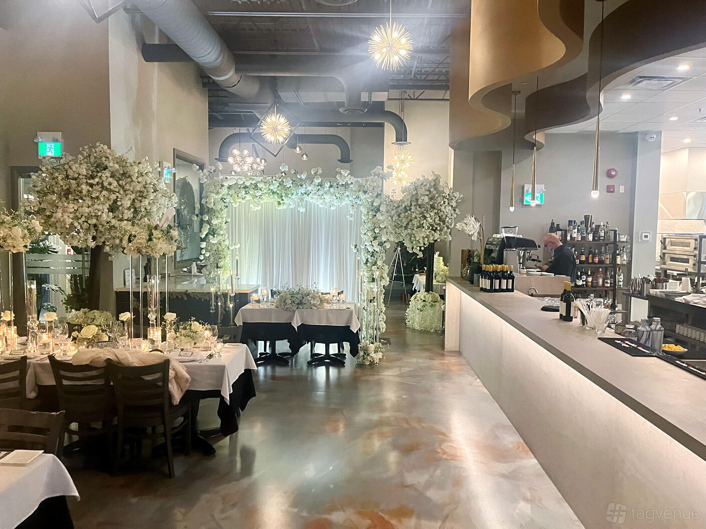 A dining room with white floral arch, velvet drapes, decorated tables, and a bar counter at Trimani Ristorante.