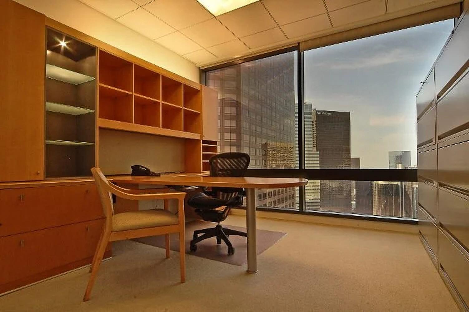 A coworking office with a large window, built-in shelving, desk, and city views at Premier Workspaces - Wells Fargo Center.