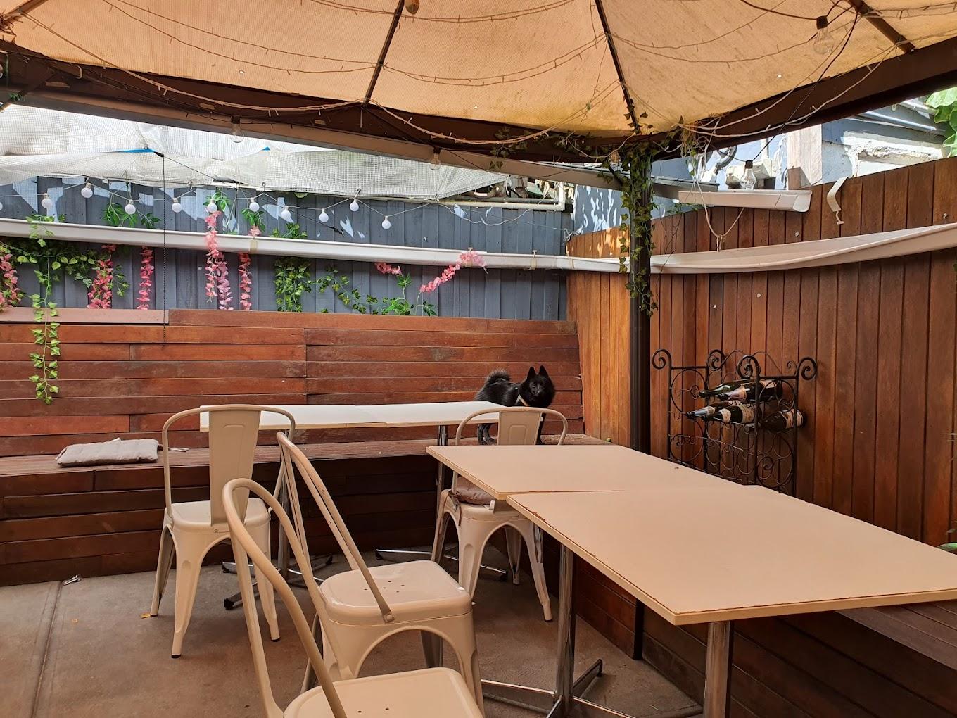 A cafe patio with wooden benches, white chairs, overhead canopy, and trailing plants at Chez Misty.