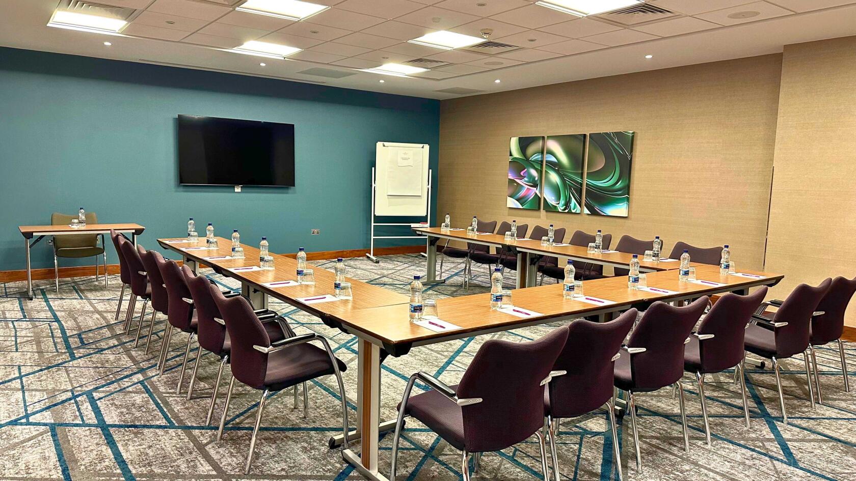 An auditorium with U-shaped tables, black chairs, bottled water, and a wall-mounted screen at Crowne Plaza Reading.