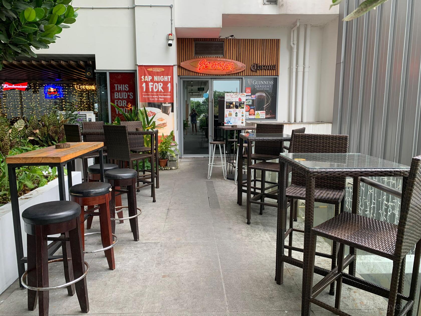 An outdoor restaurant area with wicker chairs, square and wooden tables, and potted plants at Georges Hideout @ Seletar.