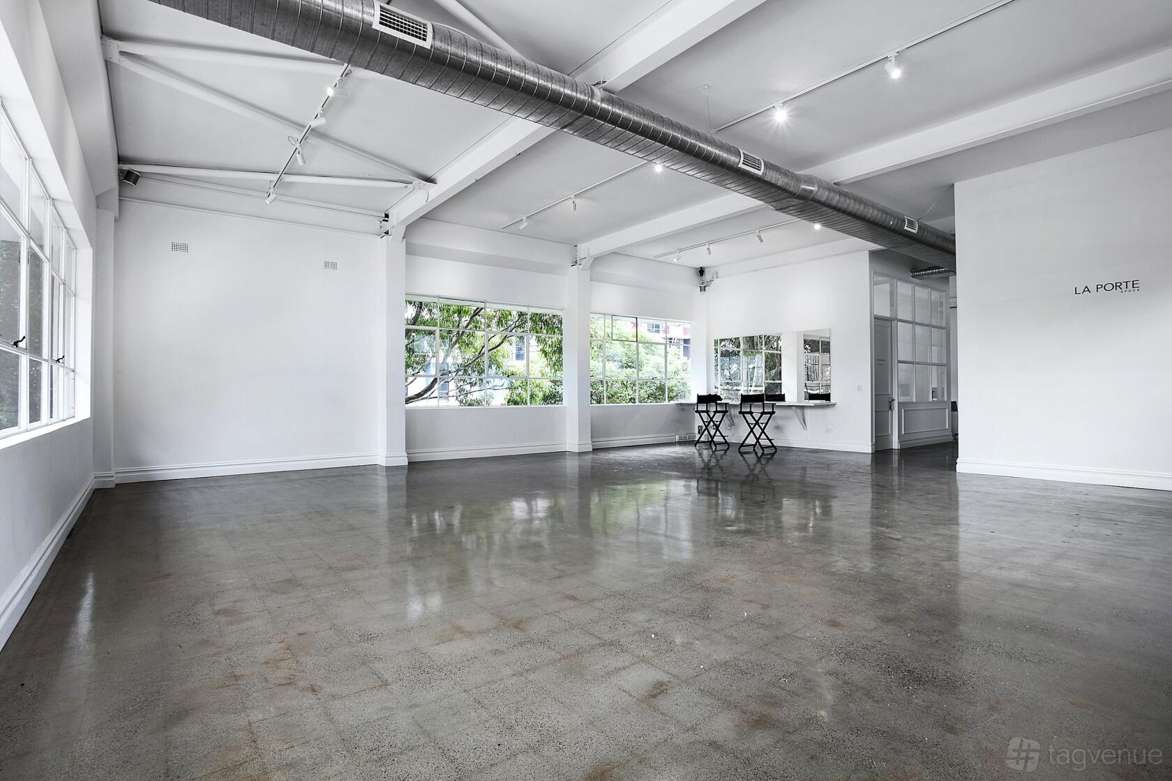 An event venue with polished concrete floors, large windows, exposed ductwork, and a wall mirror at La Porte Space.