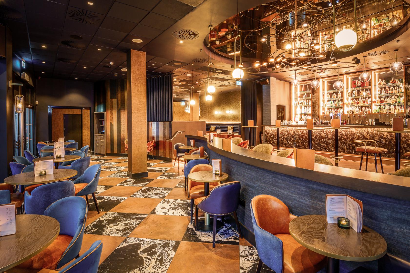 A restaurant with marble-patterned floors, plush velvet chairs, and a large illuminated bar at Gaucho O2 Arena.