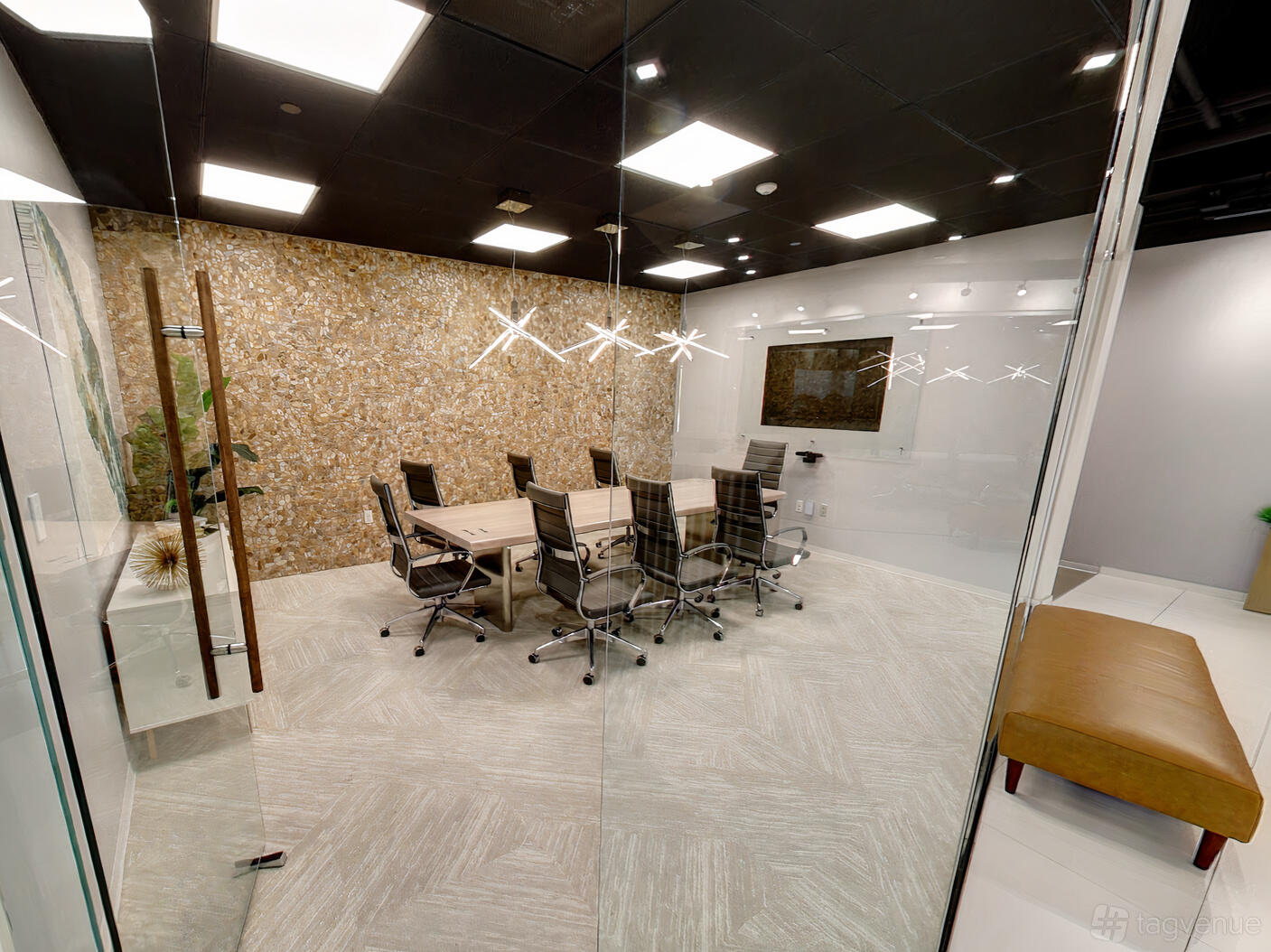A boardroom with a wood conference table, black chairs, and a stone accent wall at Lucid Private Offices - Uptown / Tanglewood.