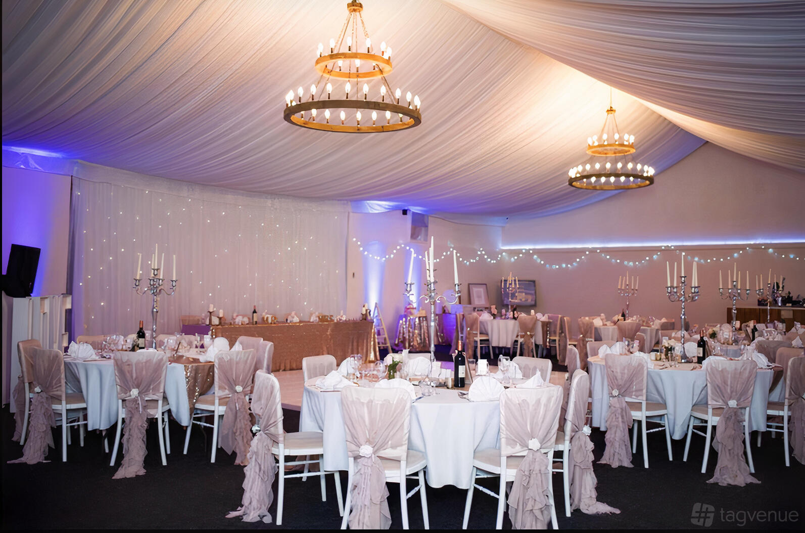 A barn with draped ceilings, round tables with blush chair covers, and chandelier lighting at Skylark Farm.