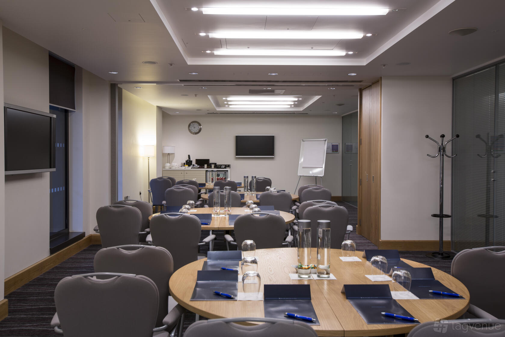 A hotel meeting room with round tables set with glassware, notepads, and a flip chart at Hilton London Heathrow Airport Terminal 5.