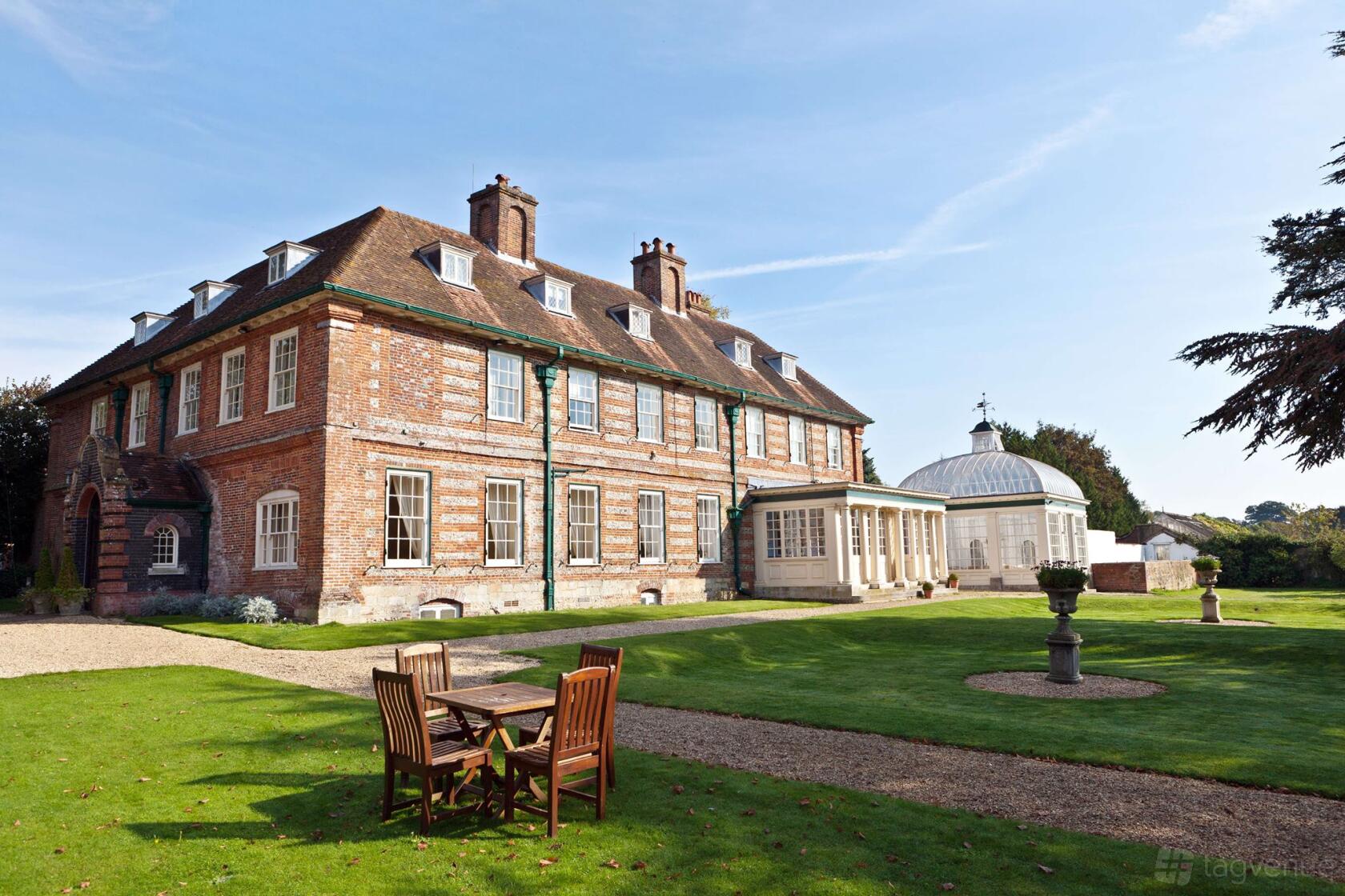 A hotel with a red brick historic manor house, white window frames, and an outdoor seating area on the lawn at Norton Park.