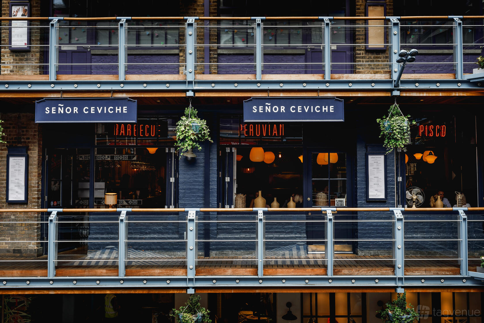 A restaurant exterior with glass balcony, hanging plants, and blue signage at Señor Ceviche Peruvian Restaurant Soho.