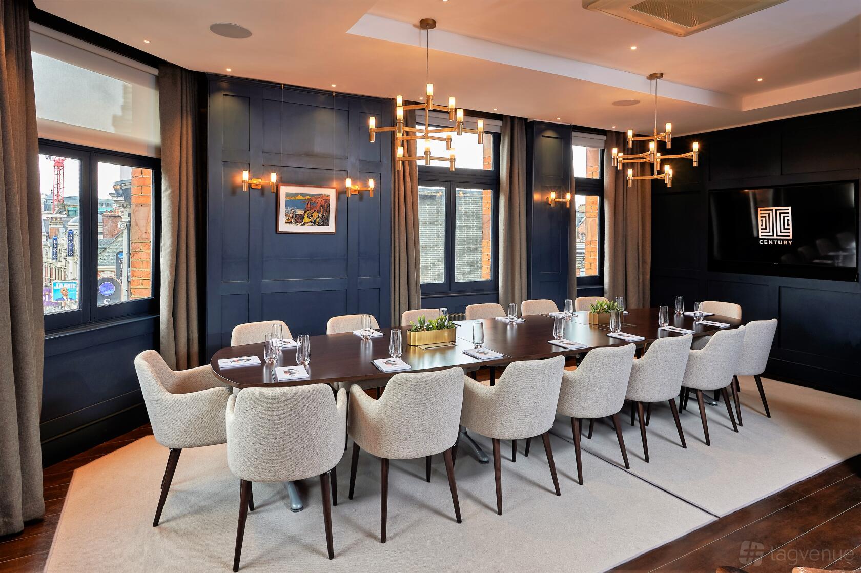 A private bar meeting room with a long dark wood table, modern chandeliers, and large windows at Century Club.