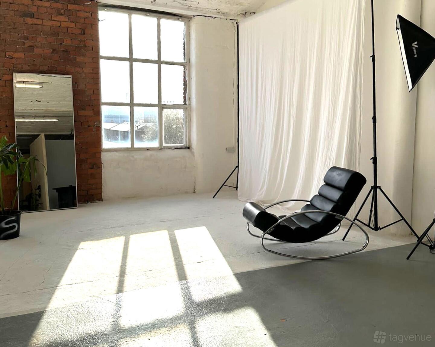 A photo studio with a large industrial window, exposed brick, and studio lighting in the Skylight Room at SPOT 1.0.1.