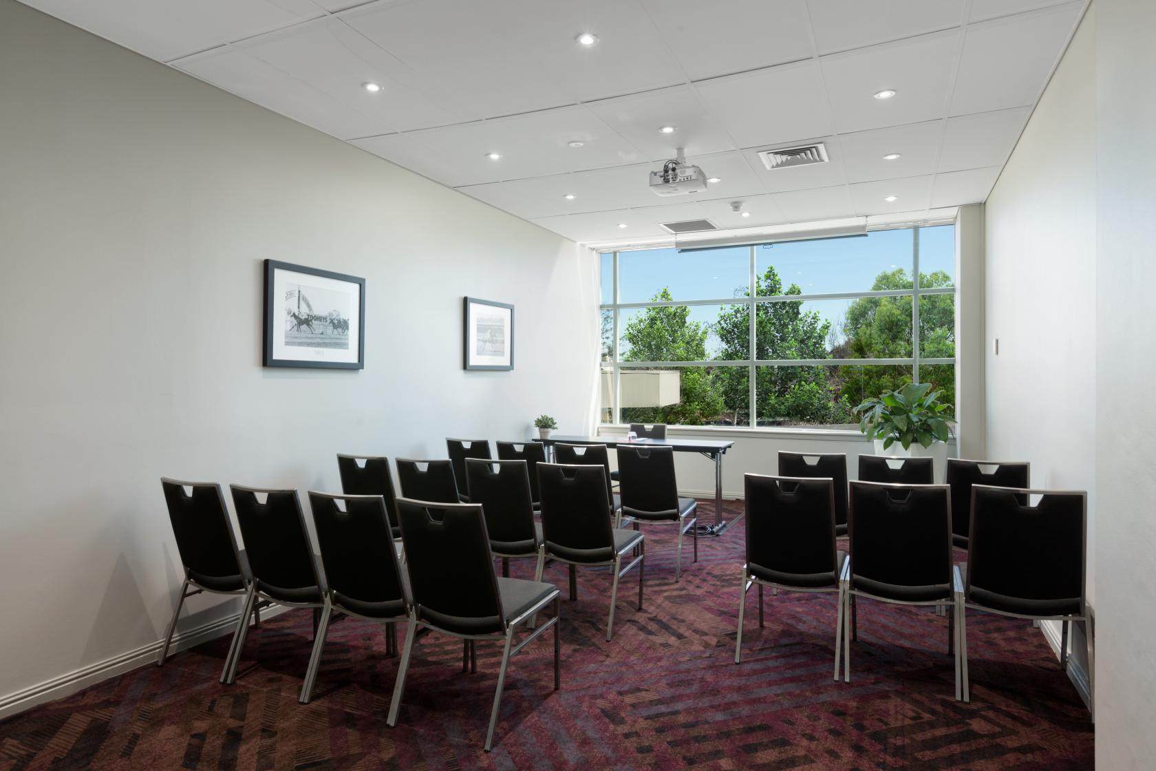 A function room with rows of black chairs, wall art, and large windows overlooking greenery at Rydges Parramatta.