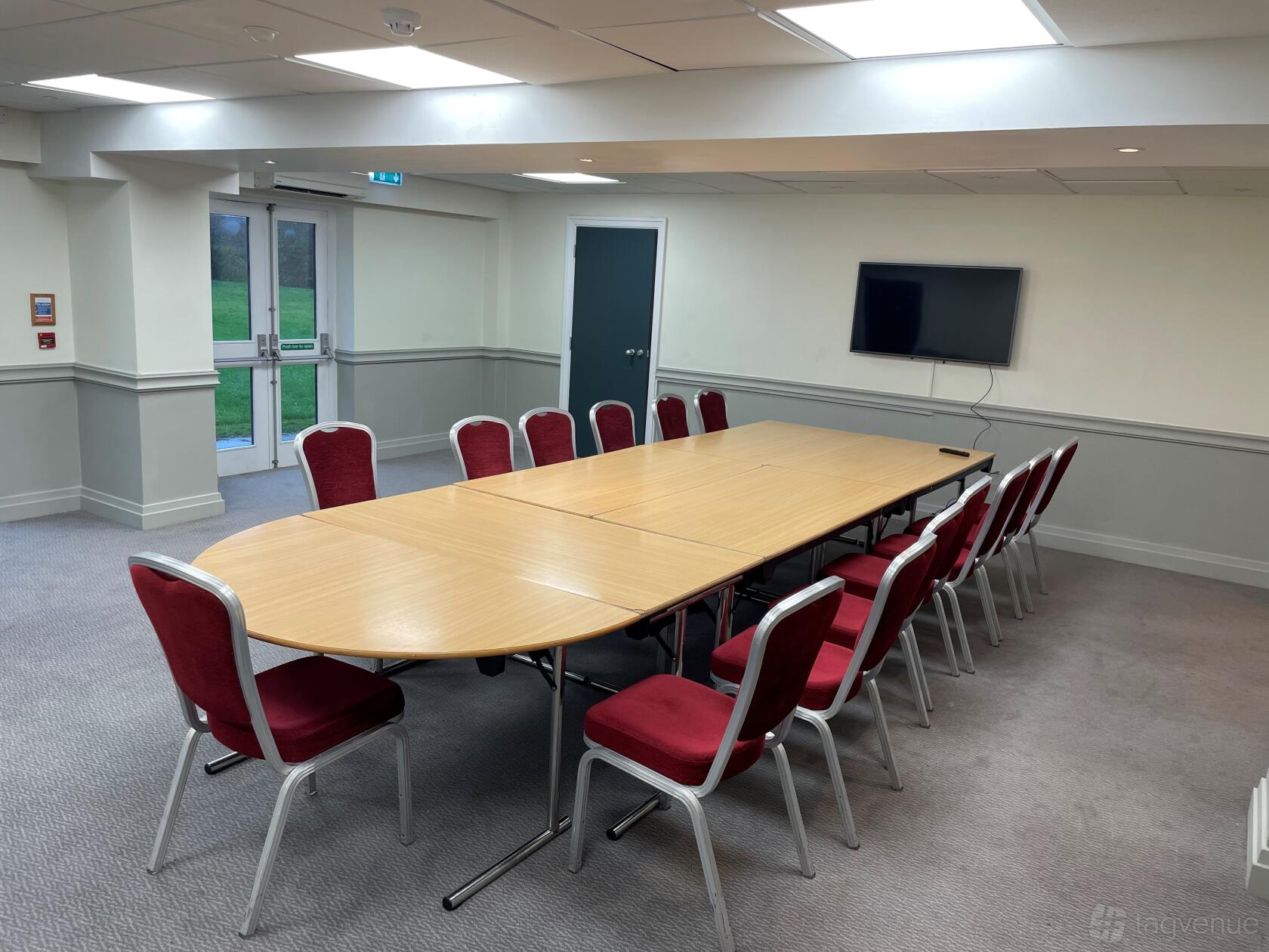 A meeting room with a U-shaped wooden table, red chairs, and wall-mounted screen at Delta Hotels by Marriott Milton Keynes.