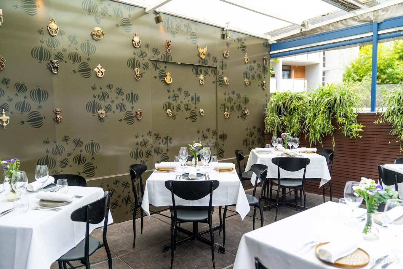 An outdoor restaurant courtyard with white tablecloths, floral centerpieces, and decorative wall art at Delhi 'O' Delhi.