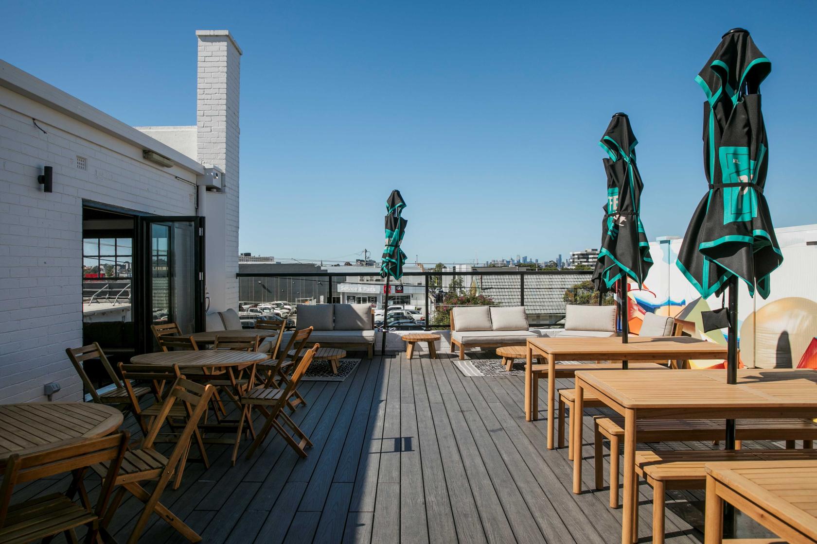 A rooftop bar with wooden tables and chairs, large umbrellas, and city views at Lulu Bar.