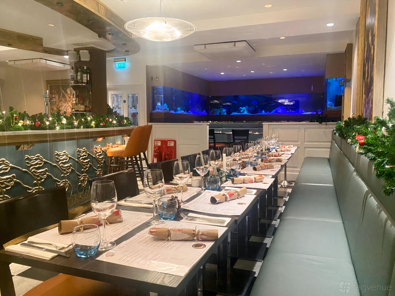 A restaurant with long banquet tables set with glassware, festive garlands, and a large aquarium at The Seashell of Lisson Grove.