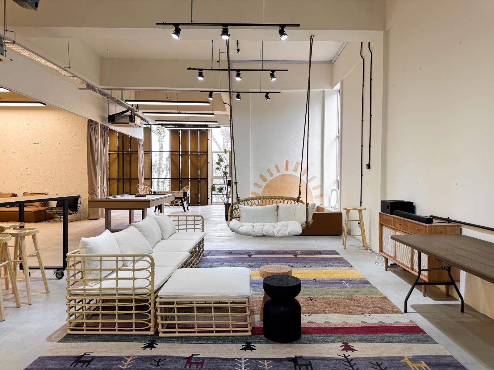 An event venue with a woven rattan sofa, colorful rug, hanging swing chair, and industrial lighting at Tinkertank - Ubi 179.