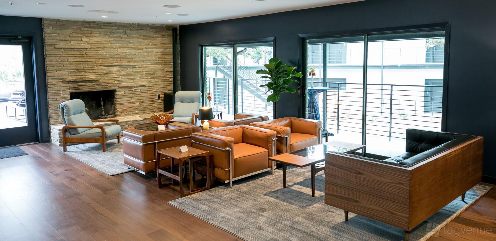 An event space with leather armchairs, stone fireplace, large windows, and potted plant at The Ruby Hotel and Bar.