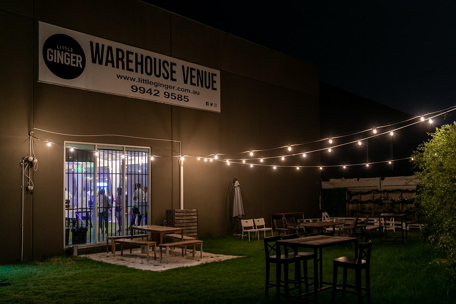 A warehouse venue with string lights, outdoor seating, and glass doors at Little Ginger Event Venue.