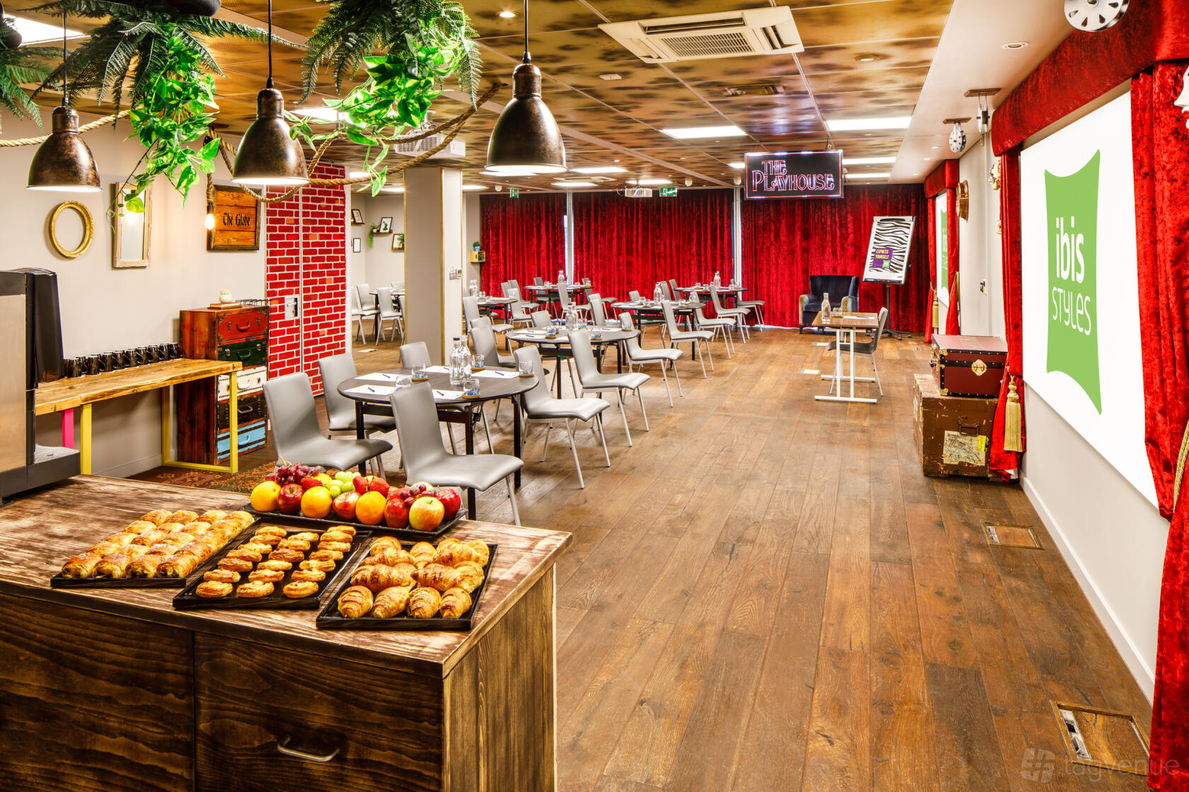A hotel ballroom with red velvet curtains, hanging pendant lights, and wooden floors at ibis Styles London Southwark.
