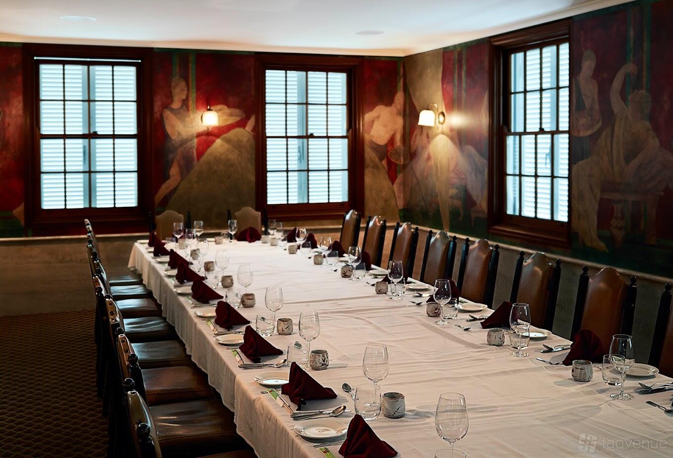 A restaurant dining room with a long banquet table set with white linens, wine glasses, and leather chairs at Blue Angel.