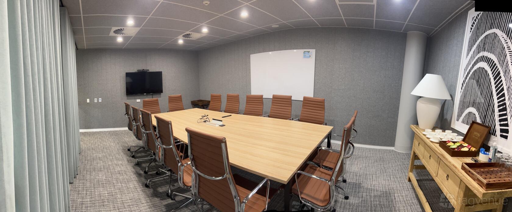 A boardroom with a long wooden conference table, leather chairs, wall-mounted screen, and whiteboard at @Workspaces - Milton.