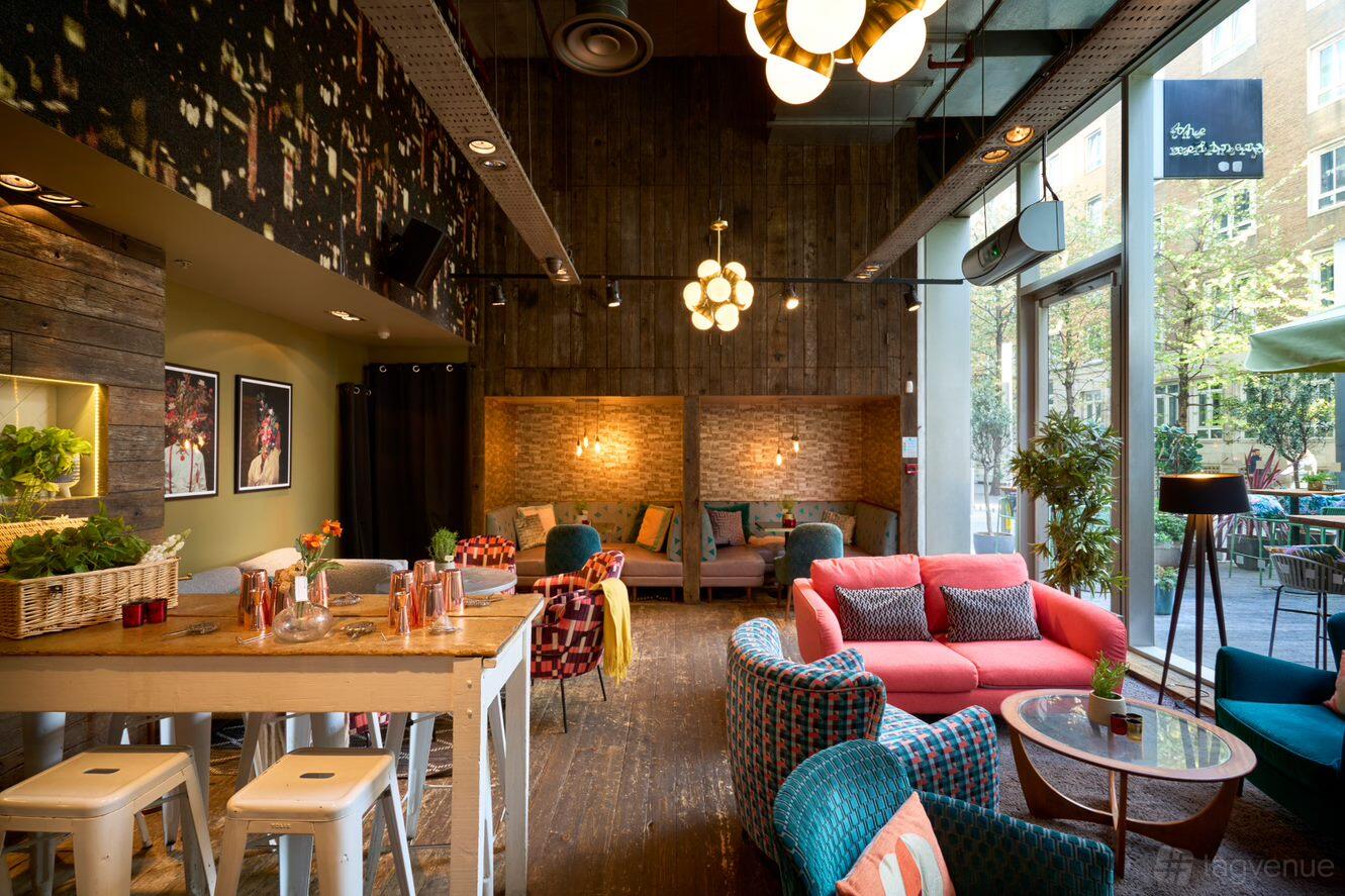 A restaurant lounge with colorful armchairs, exposed brick walls, and floor-to-ceiling windows at The Refinery Bankside.