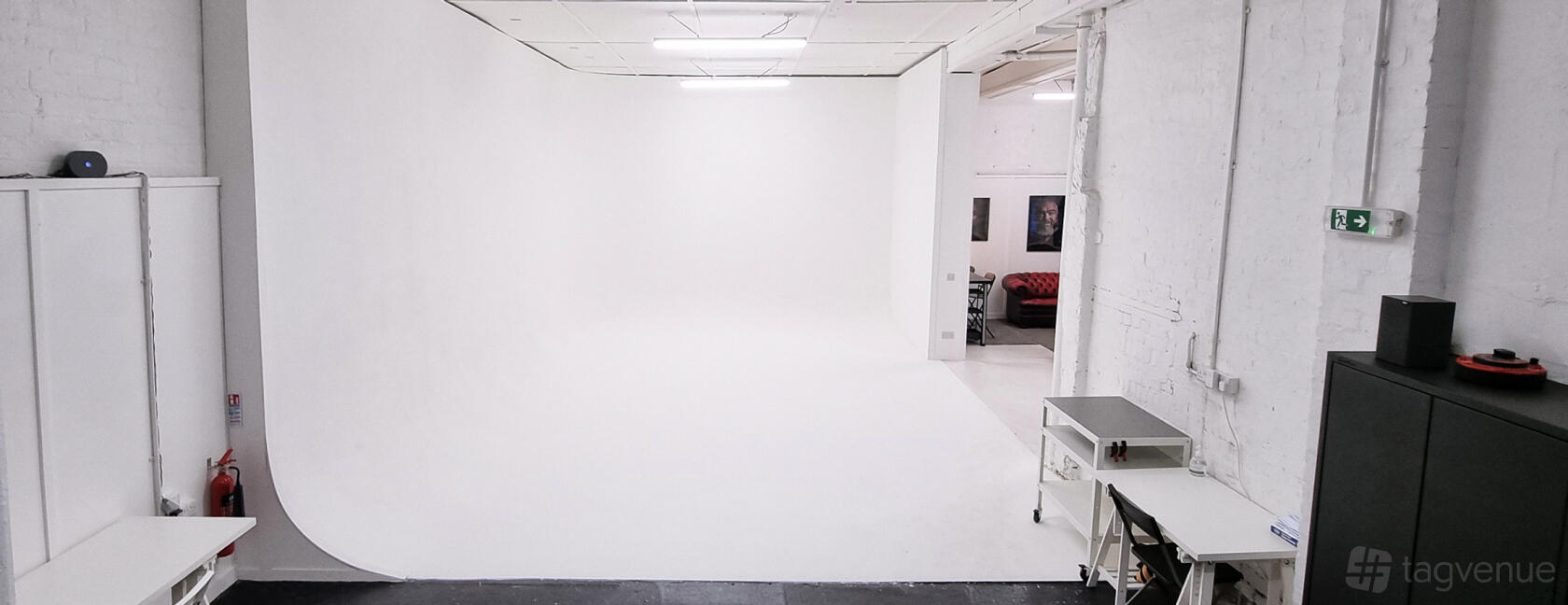 A photo studio with a white infinity cove backdrop, overhead lighting, and a small work desk at Cove One Studios.