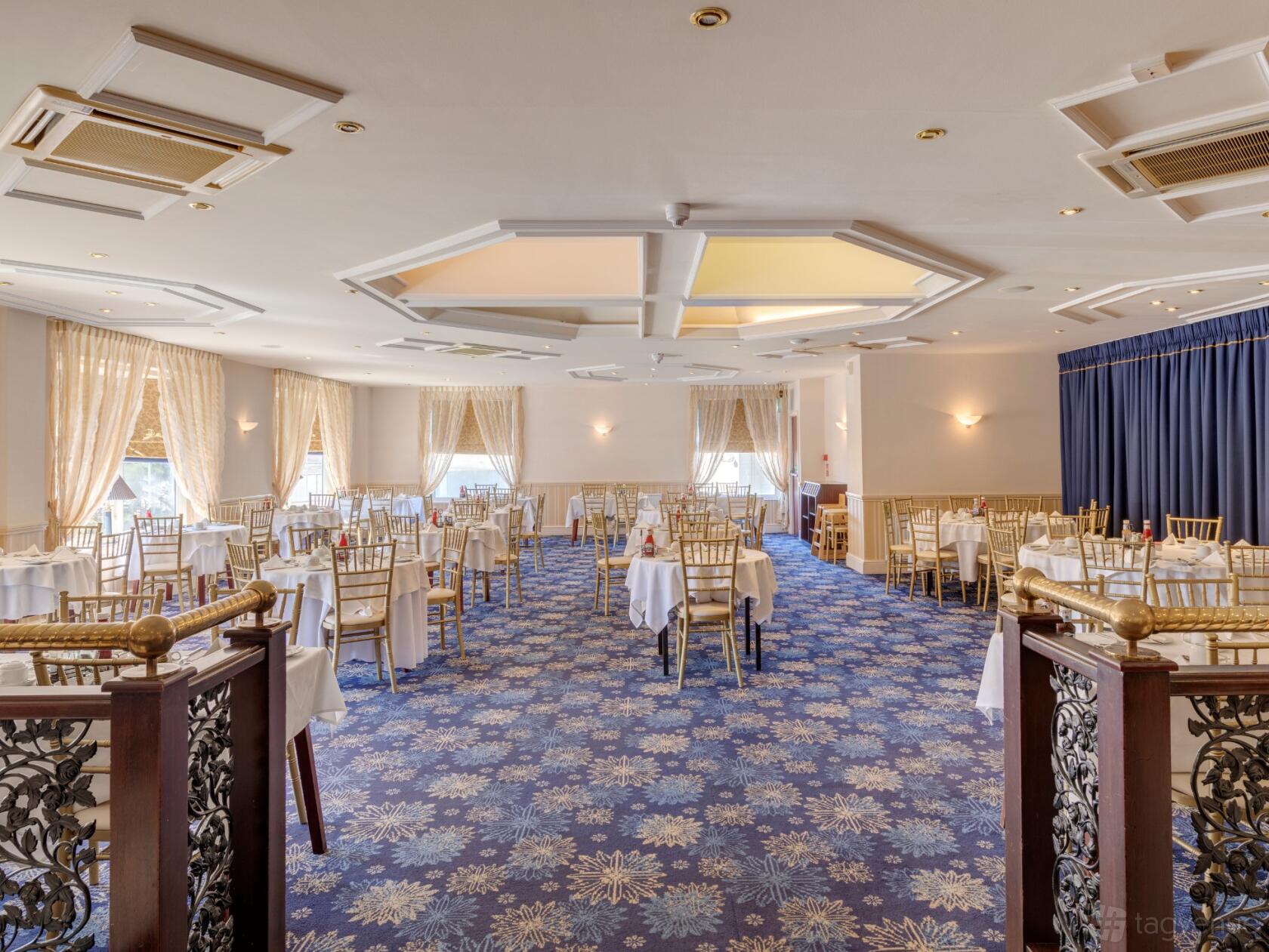 An event space with round tables, gold chairs, blue patterned carpet, and large windows at New Continental Hotel.
