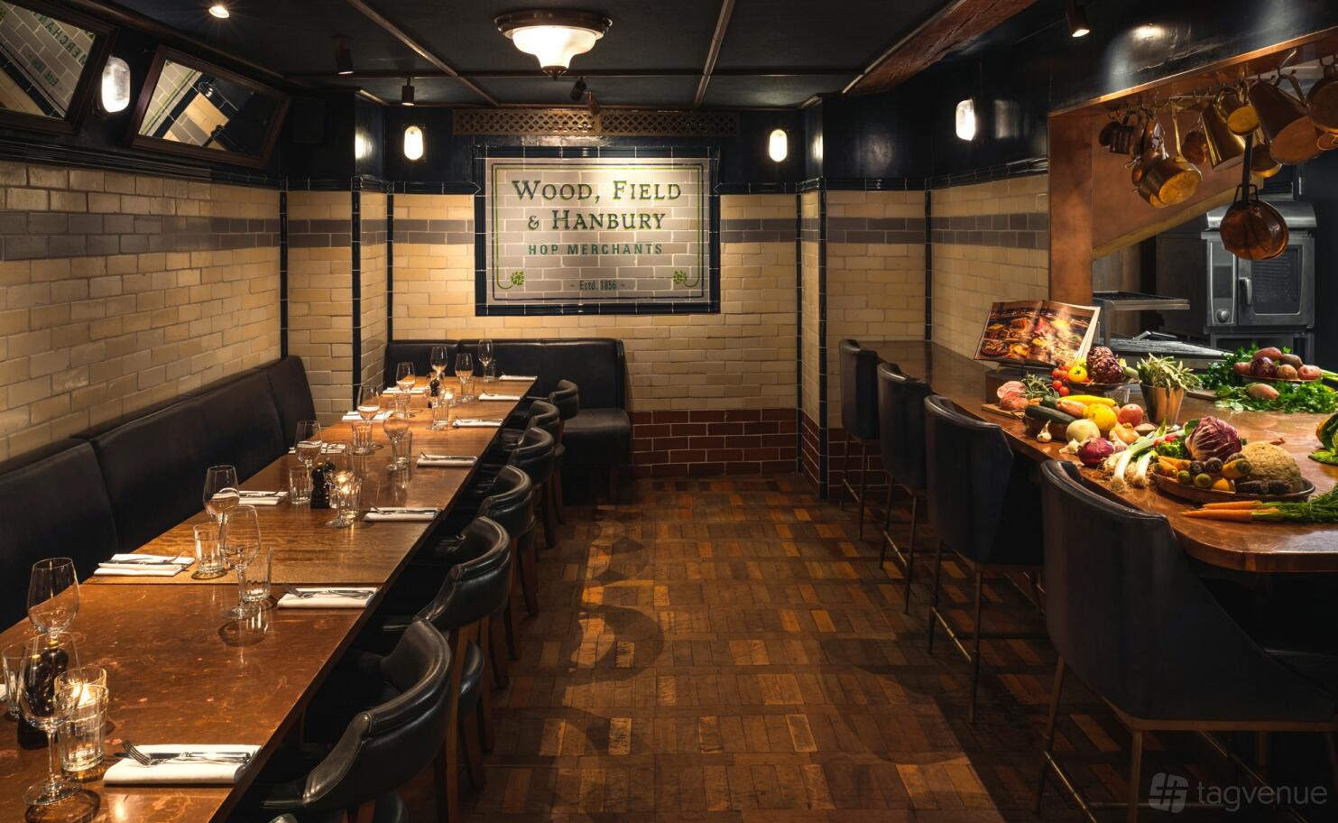 A dining room with tiled walls, a long wooden table, leather chairs, and an open counter with fresh produce at Hawksmoor Borough.