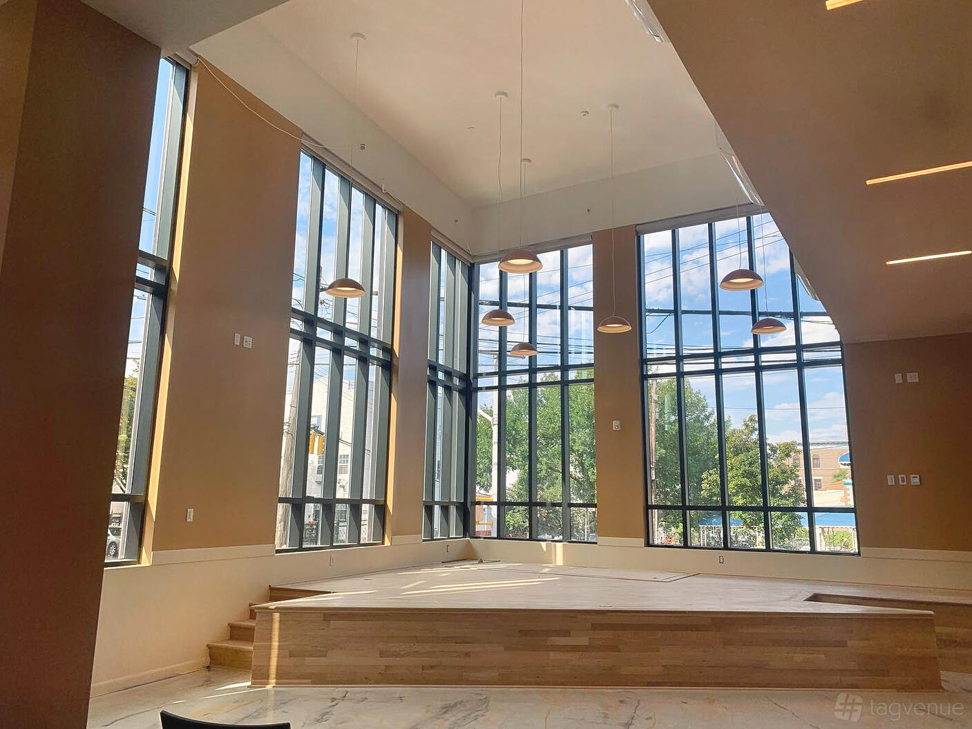 An event venue with floor-to-ceiling windows, high ceilings, and a raised wooden stage at The Haven on Home Street.