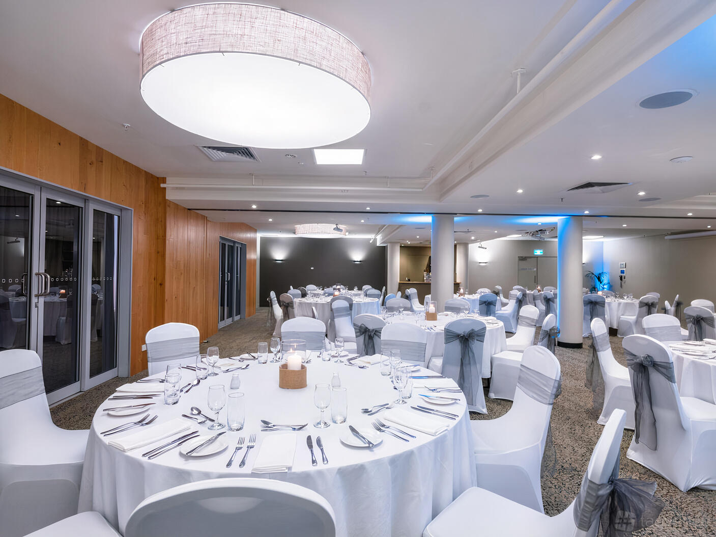 An event space with round tables dressed in white linens and grey chair sashes at The Old Woolstore Apartment Hotel.