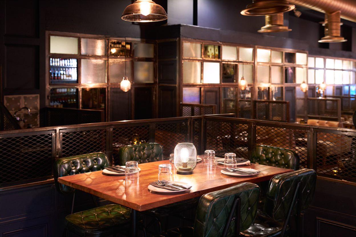 An event space in a restaurant with a wooden table, green leather chairs, glassware, and pendant lighting at The Last Talisman.